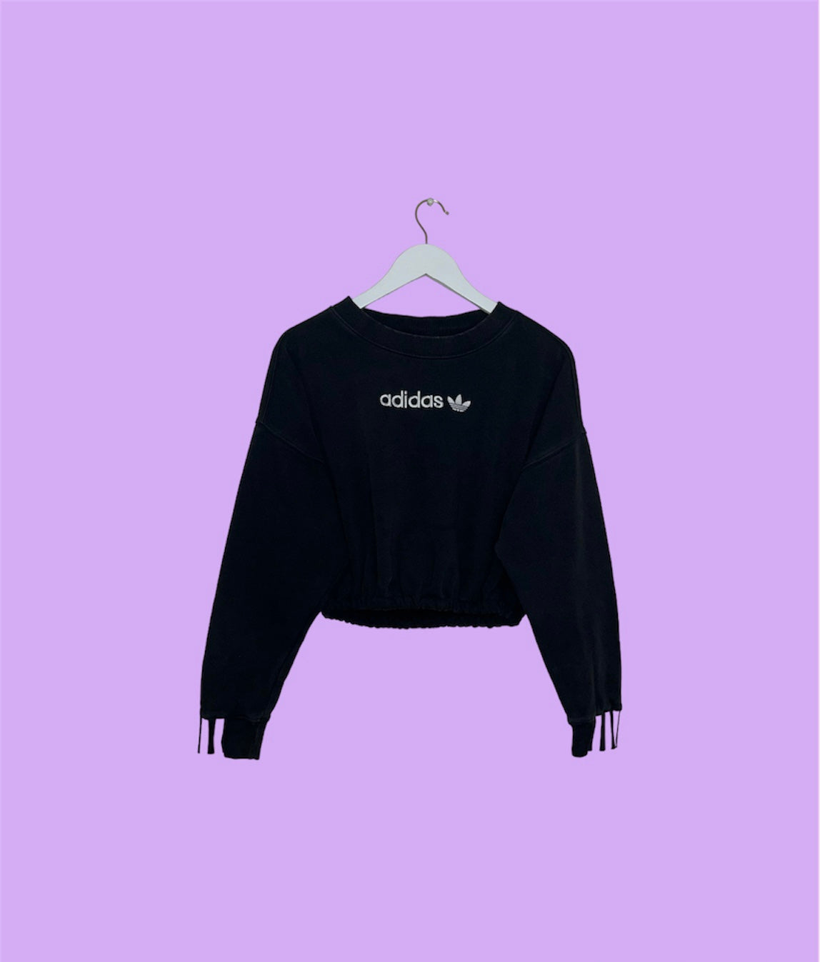 black cropped sweatshirt with white adidas logo shown on a lilac background