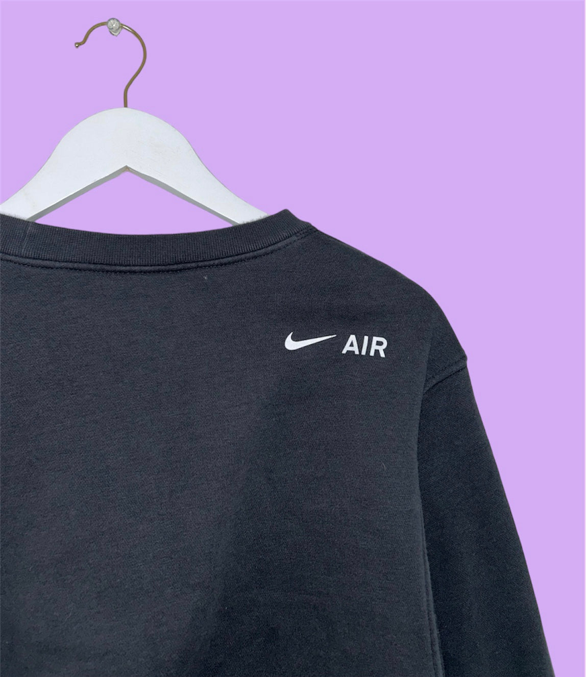 back of a black cropped sweatshirt with white nike air logo shown on a lilac background