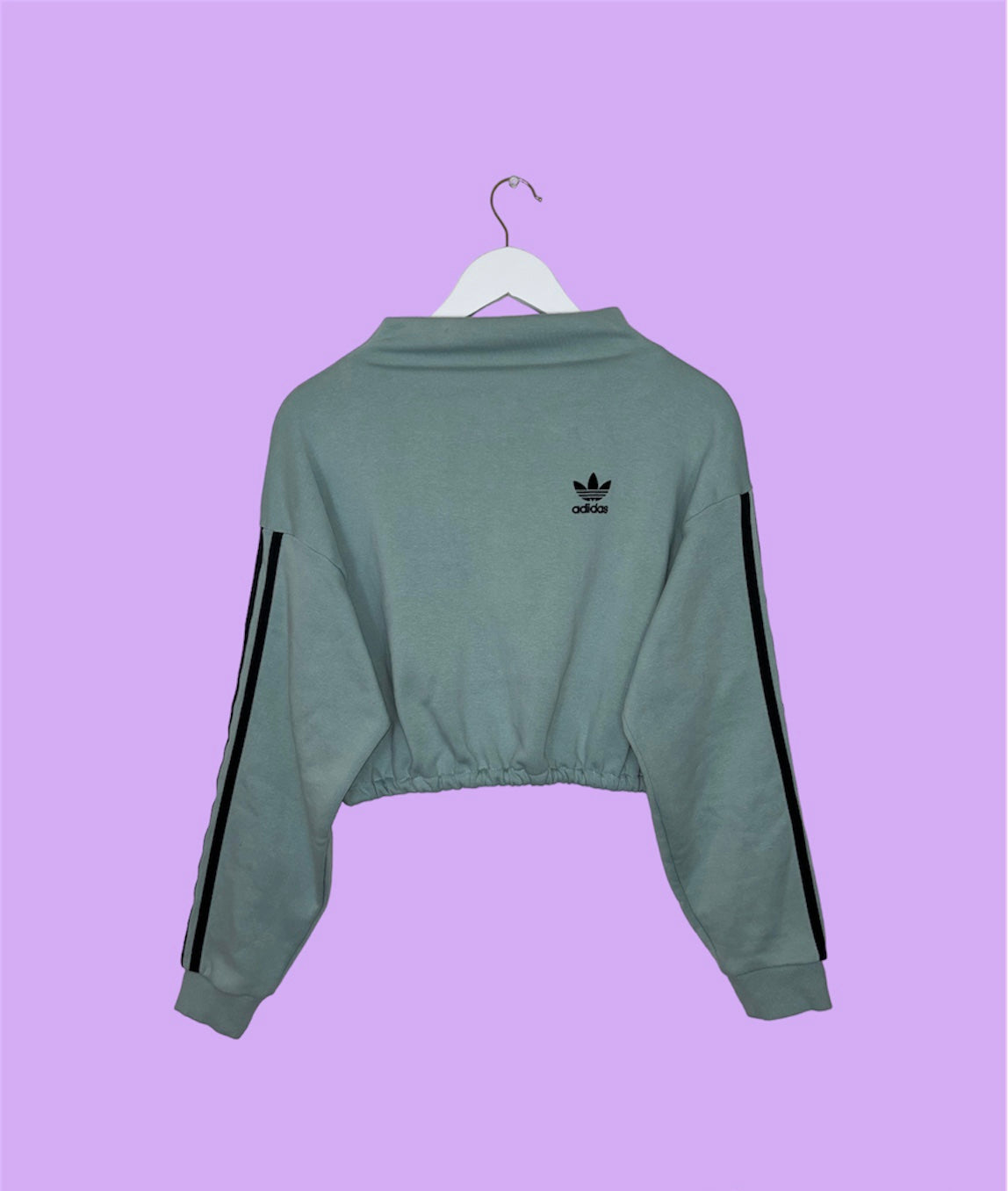 light blue cropped sweatshirt with black adidas logo shown on a lilac background