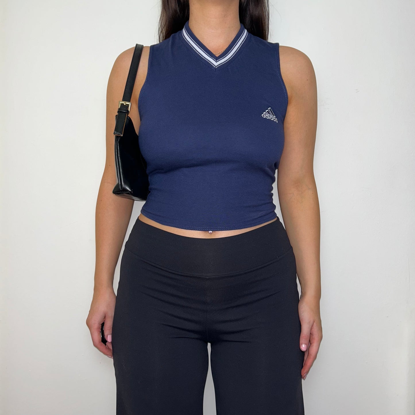 navy sleeveless crop top with white adidas logo shown on a model wearing black trousers and a black shoulder bag
