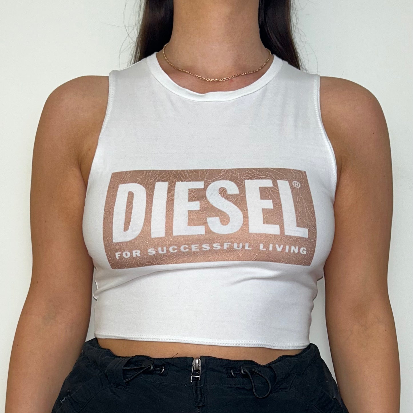 close up of white sleeveless crop top with pink and white diesel logo shown on a model wearing a black mini skirt