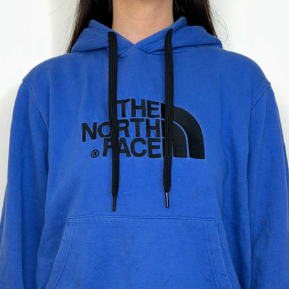close up of blue hoodie with black north face logo shown on a model wearing a blue denim mini skirt