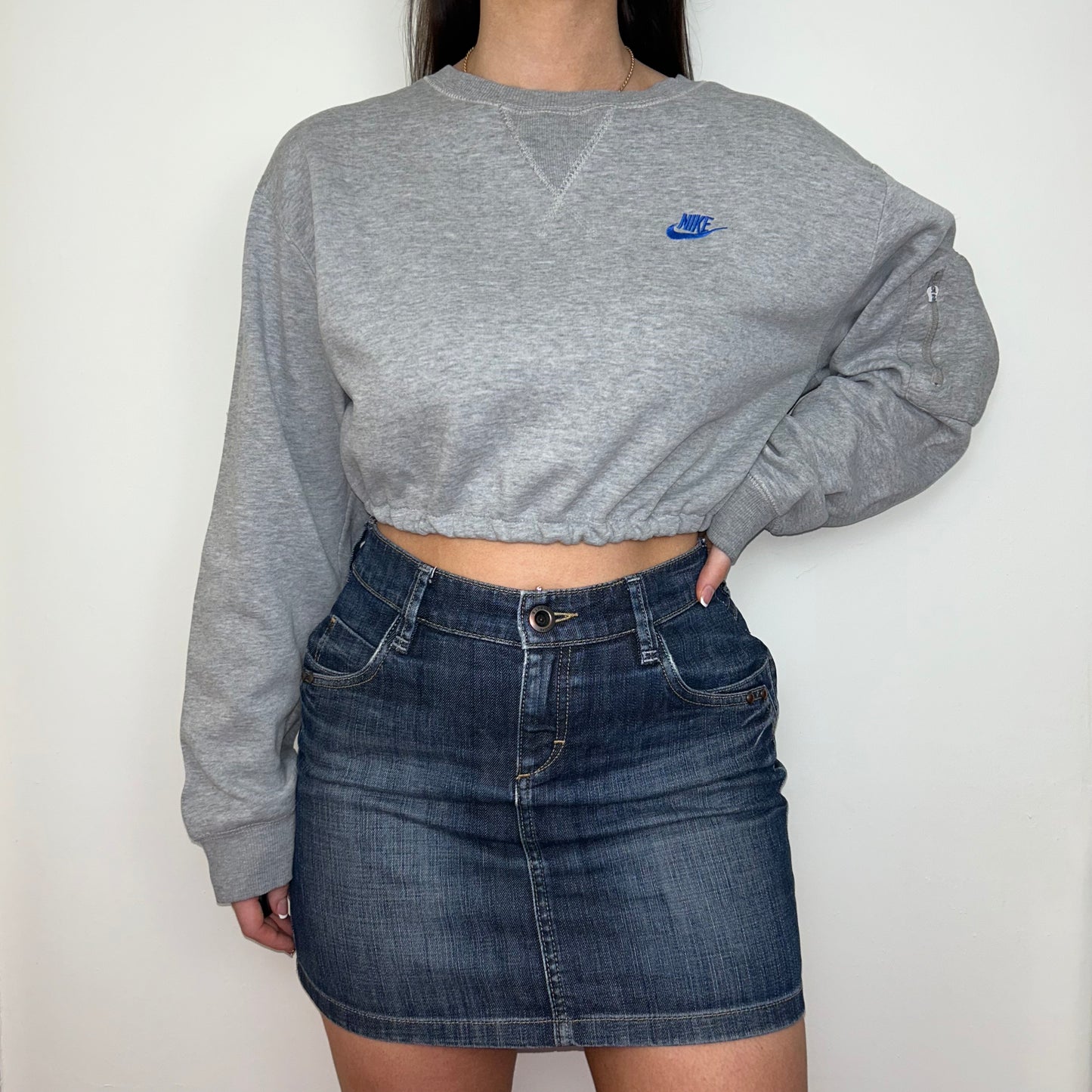 grey cropped sweatshirt with blue nike logo shown on a model wearing a blue denim mini skirt