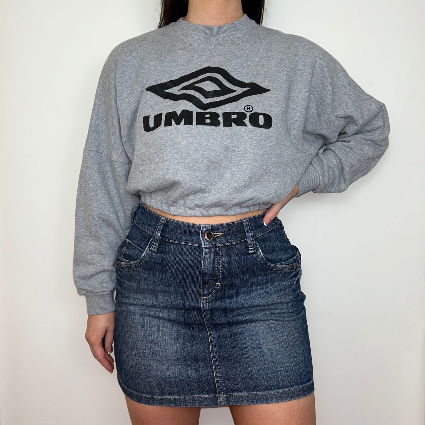 light grey cropped sweatshirt with black umbro logo shown on a model wearing a blue denim mini skirt