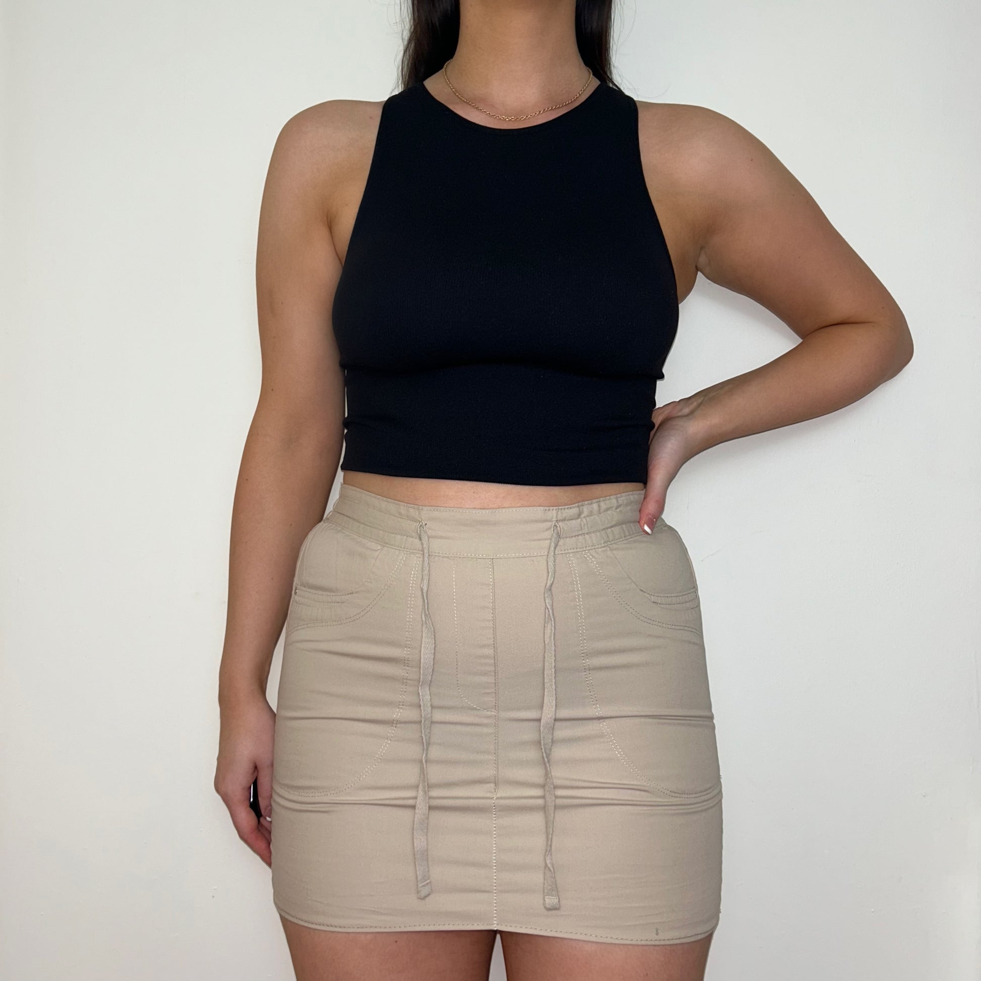 beige mini cargo skirt shown on a model wearing a black sleeveless crop top