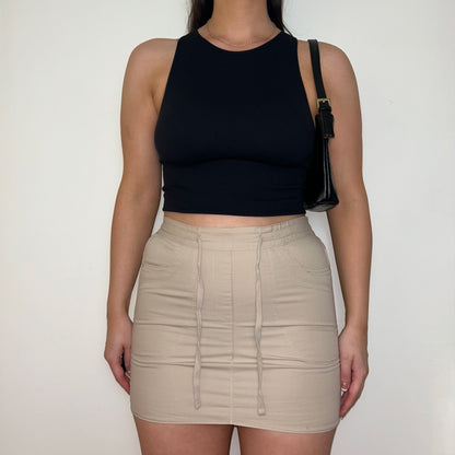 beige mini cargo skirt shown on a model wearing a black sleeveless crop top and black shoulder bag