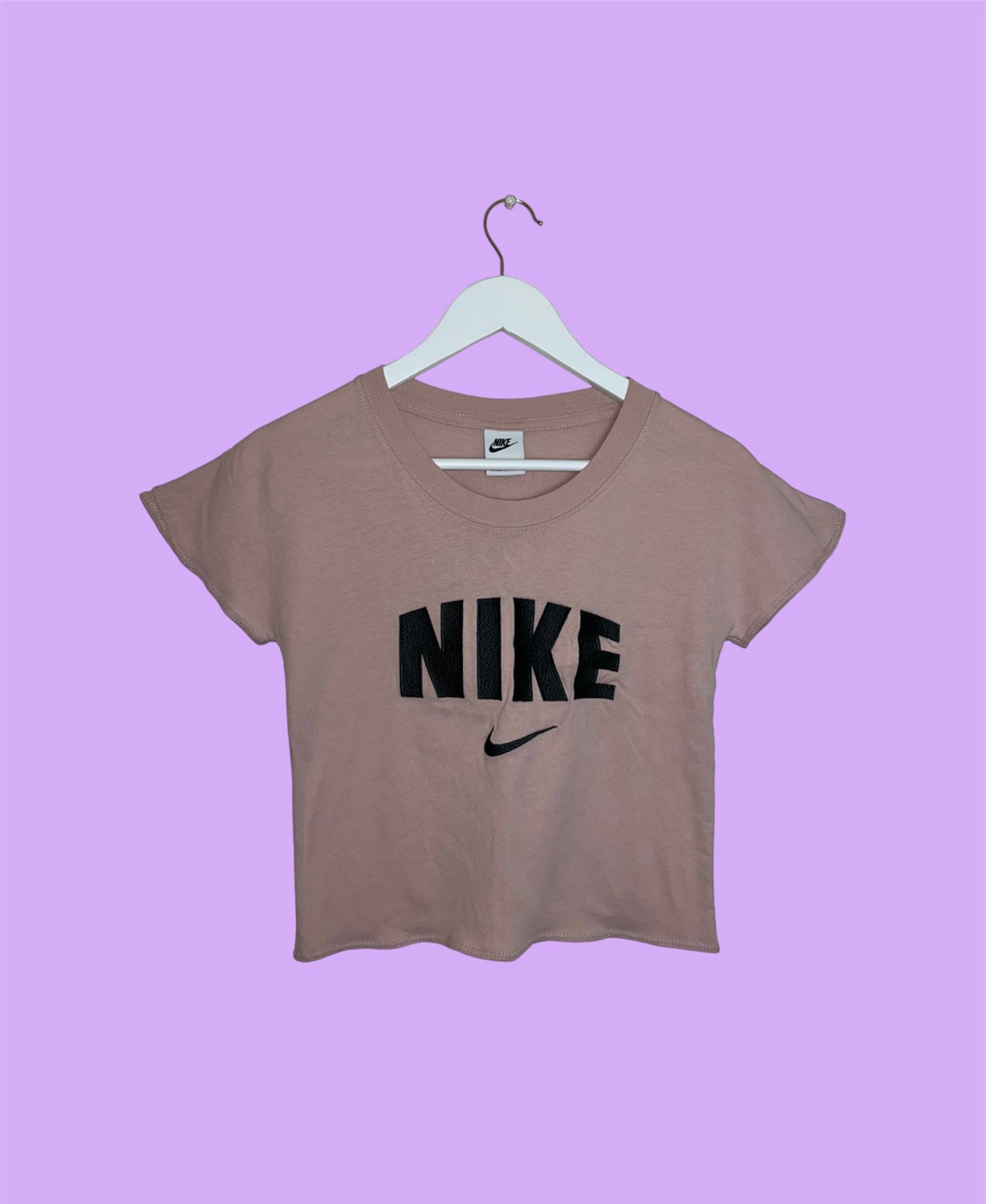 light pink short sleeve crop top with black nike logo shown on a lilac background