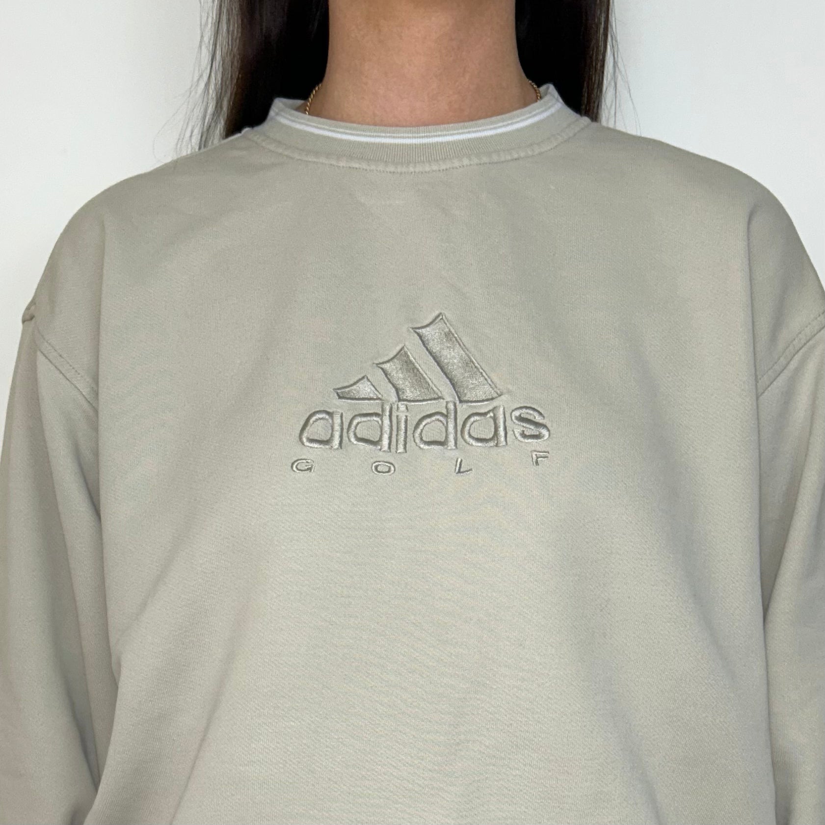 close up of beige sweatshirt with adidas golf logo shown on a model