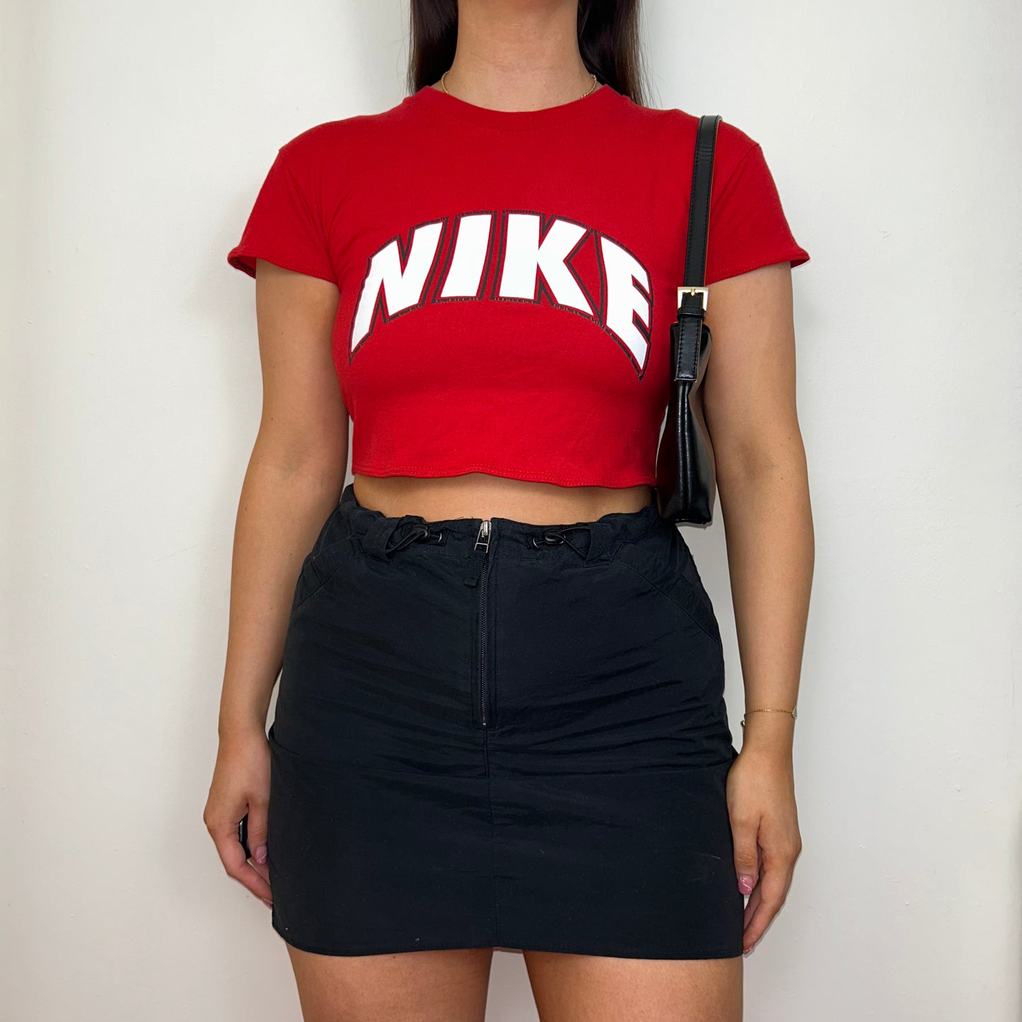 red short sleeve crop top with white nike logo shown on a model wearing a black skirt and black shoulder bag