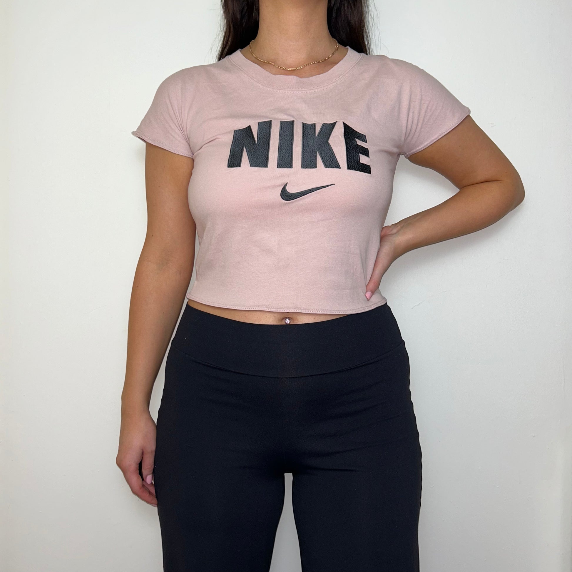 light pink short sleeve crop top with black nike logo shown on a model wearing black trousers