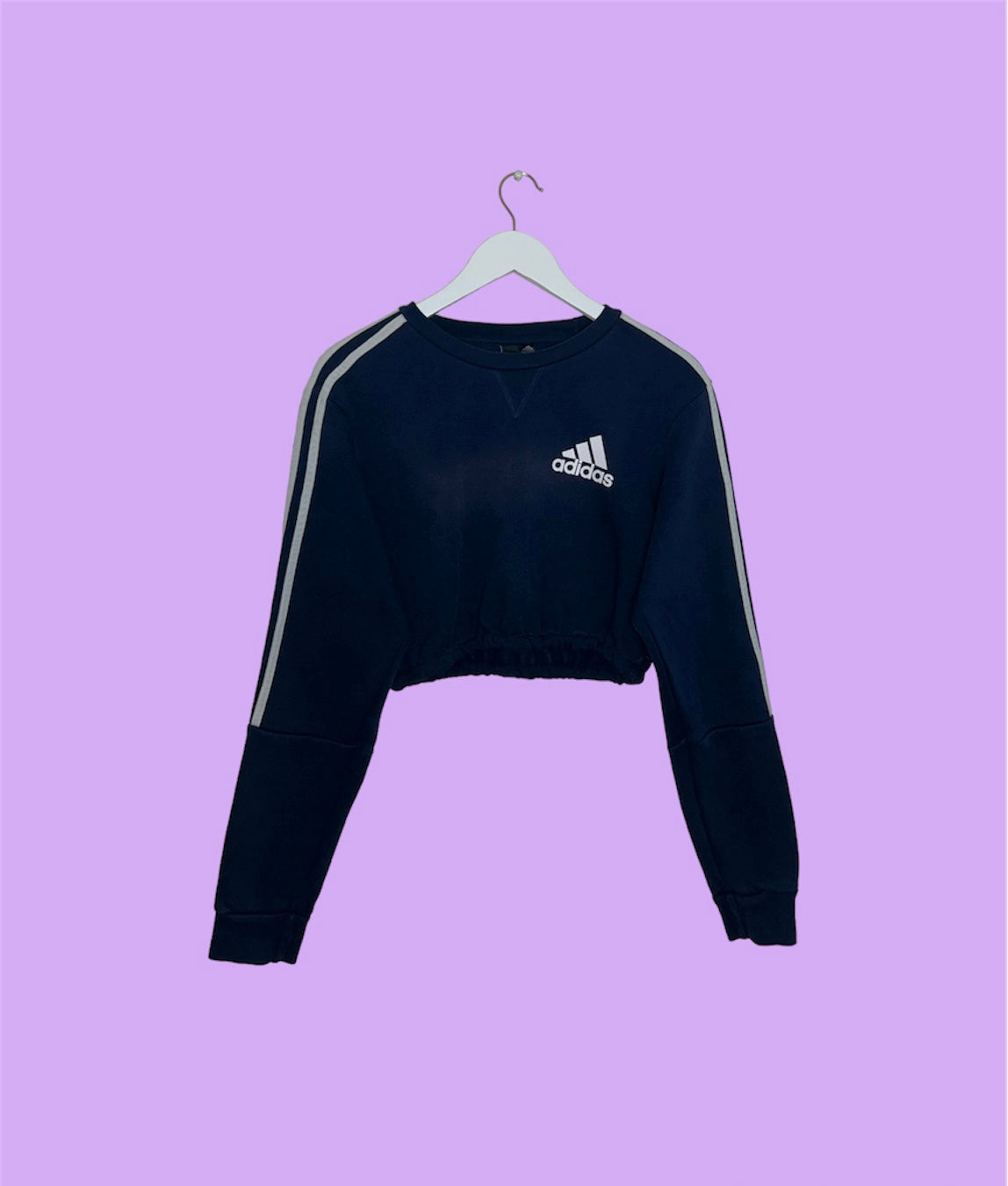 navy cropped sweatshirt with white adidas logo shown on a lilac background
