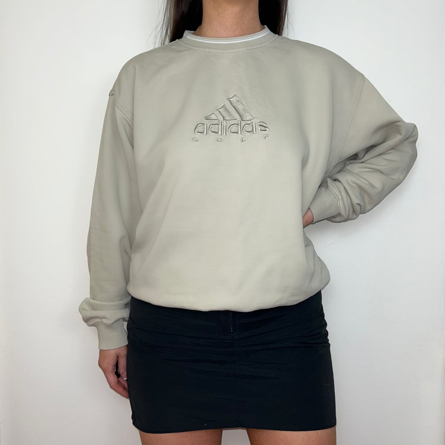 beige sweatshirt with adidas golf logo shown on a model wearing a black mini skirt