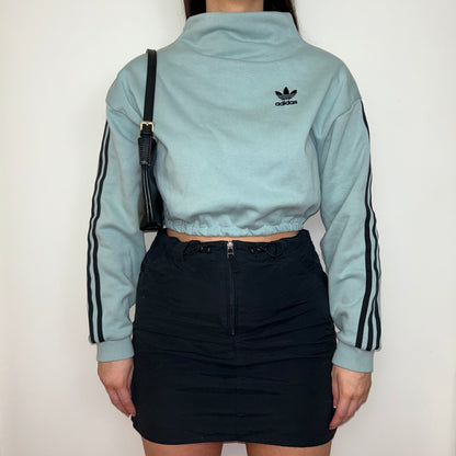 light blue cropped sweatshirt with black adidas logo shown on a model wearing a black mini skirt and black shoulder bag