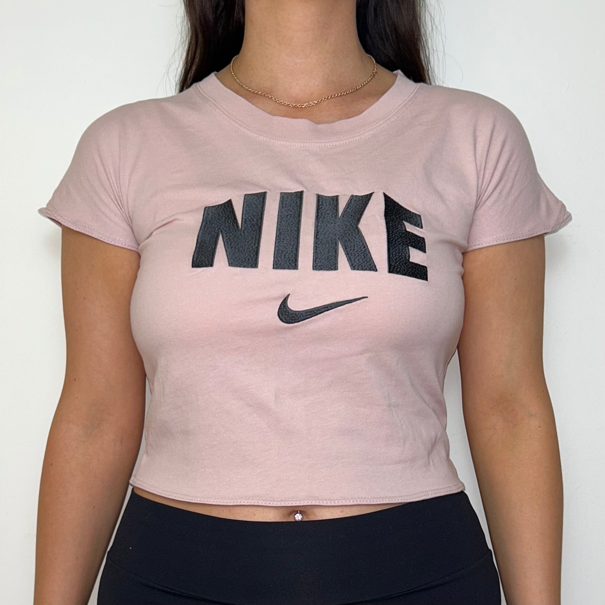 close up of light pink short sleeve crop top with black nike logo shown on a model wearing black trousers