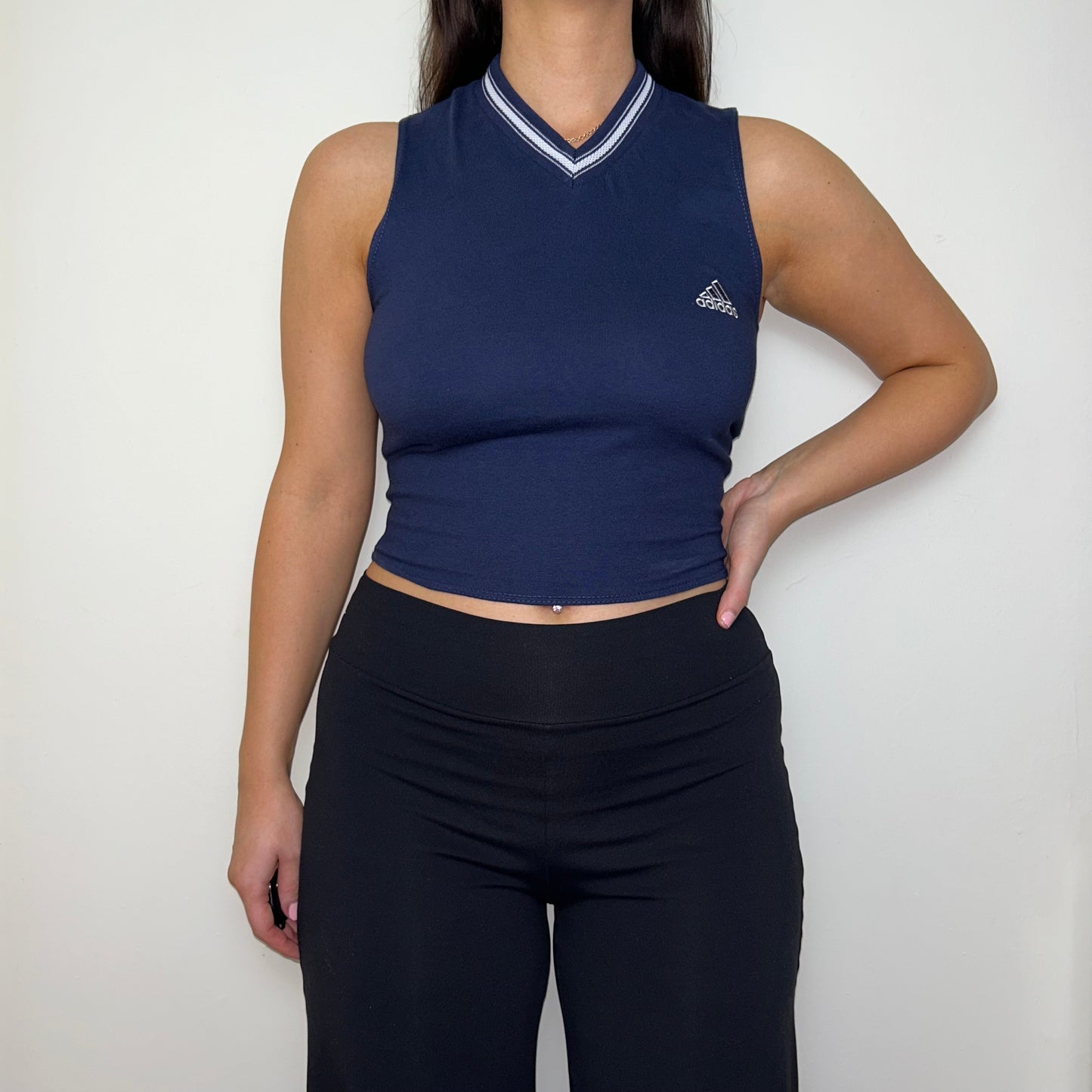 navy sleeveless crop top with white adidas logo shown on a model wearing black trousers