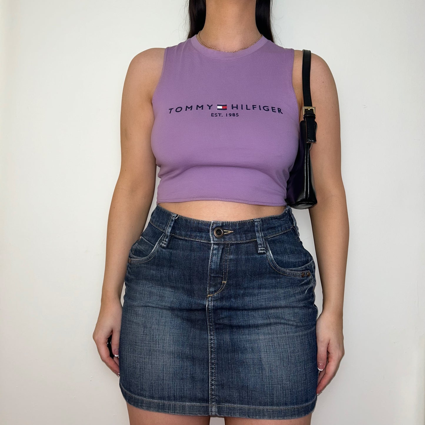 lilac sleeveless crop top with black tommy hilfiger logo shown on a model wearing a denim mini skirt and black shoulder bag