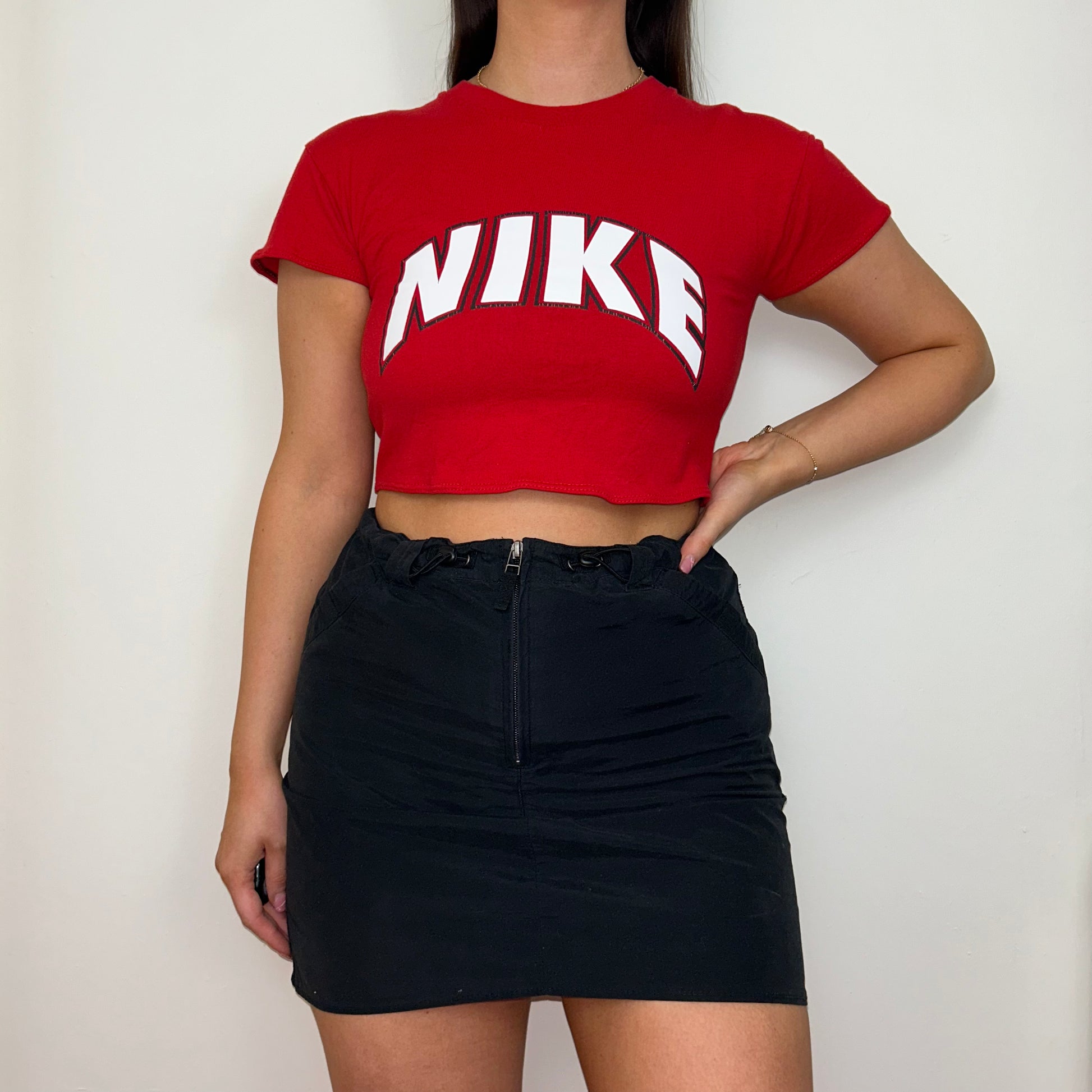 red short sleeve crop top with white nike logo shown on a model wearing a black skirt