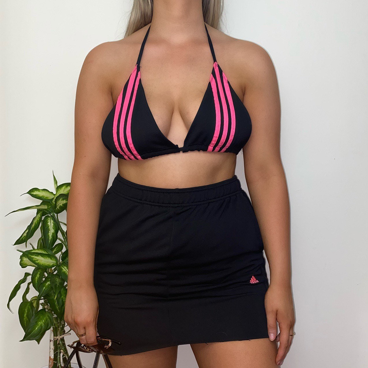 model wearing adidas triangle bikini crop top with hot pink 3 stripe detail and matching black skirt with small pink adidas logo