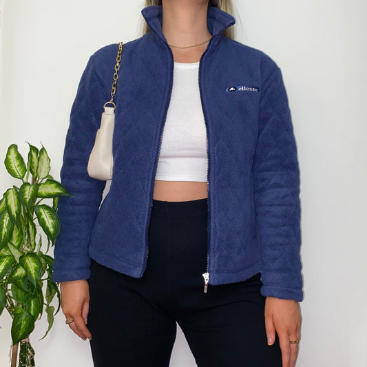 navy zip ellesse jacket with embroidered text logo on chest shown on model wearing white crop top and black trousers with gold chain white shoulder bag