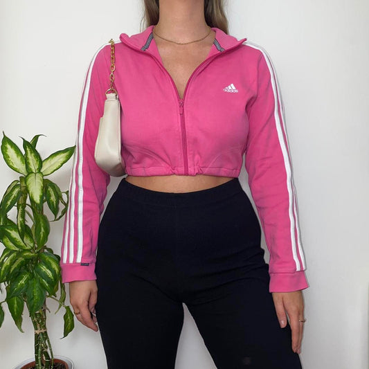bright pink cropped jumper with small white Adidas text and symbol logo on chest shown on a model wearing black trousers and gold chain shoulder bag