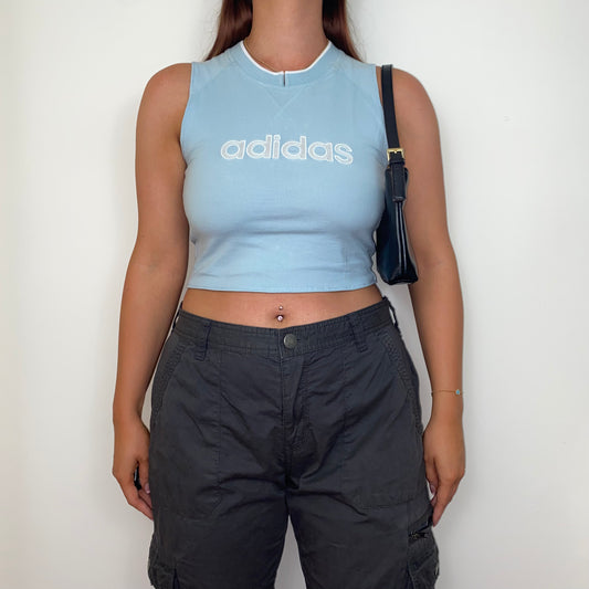 light blue sleeveless crop top with white adidas logo shown on a model wearing grey trousers and a black shoulder bag