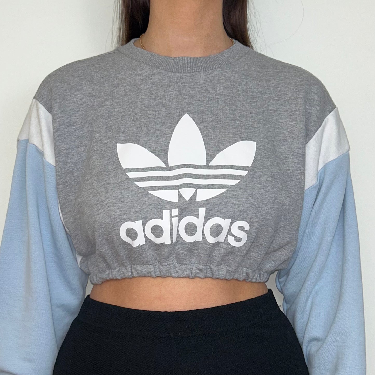 close up of grey and blue cropped sweatshirt with white adidas logo shown on a model