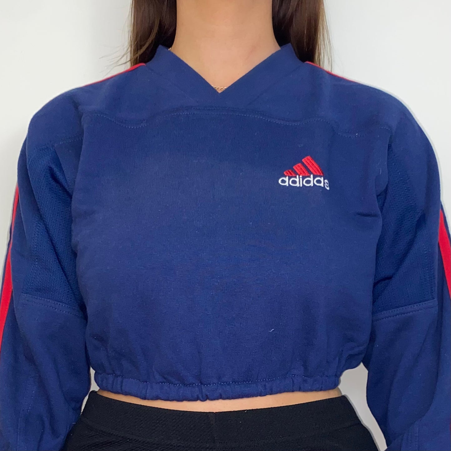 close up of navy cropped sweatshirt with red adidas logo shown on a model wearing black trousers