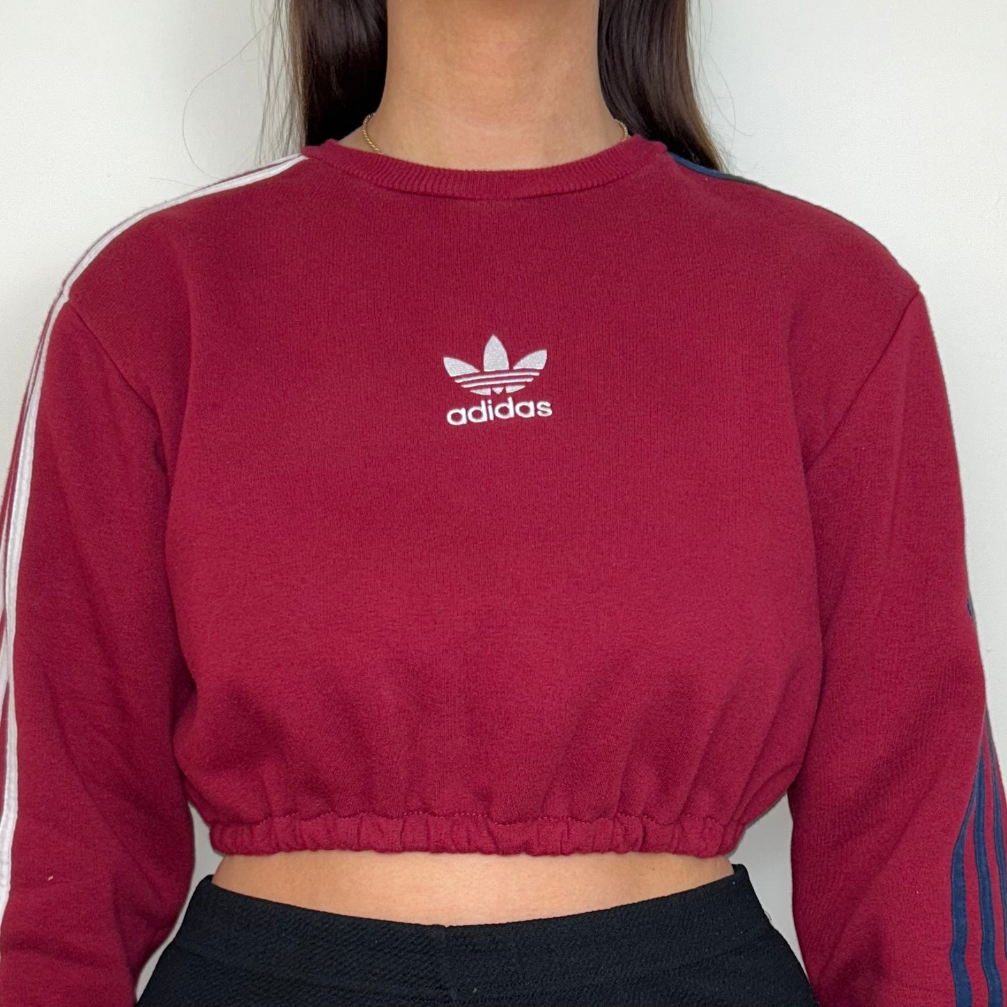 close up of burgundy cropped sweatshirt with white adidas logo shown on a model