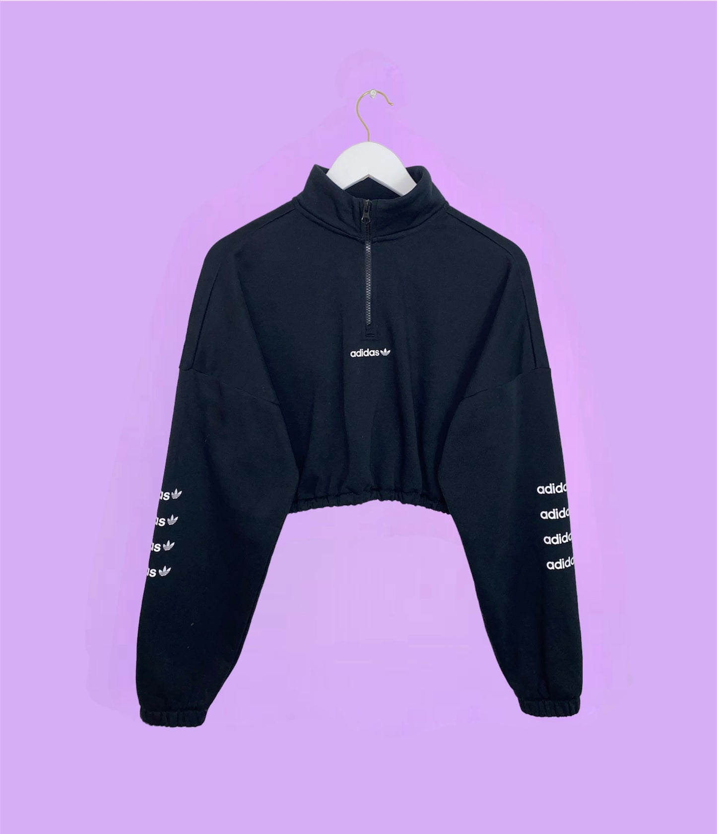 black 1/4 zip cropped sweatshirt with white adidas logo on front and sleeves shown on a lilac background