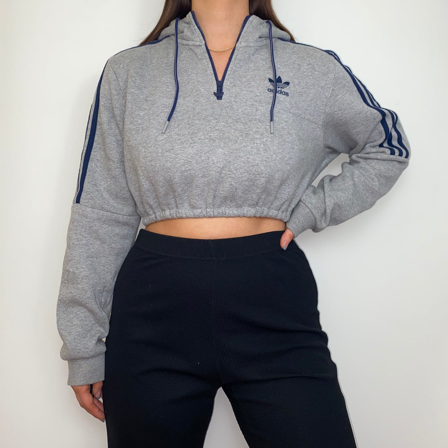 grey 1/4 zip cropped hoodie with navy adidas logo shown on a model wearing black trousers with hand on hip