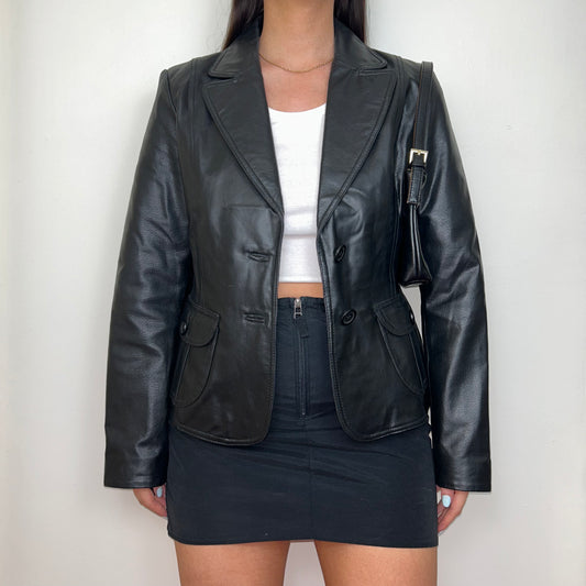 black real leather blazer jacket shown on a model wearing a white crop top and black mini skirt with a black shoulder bag