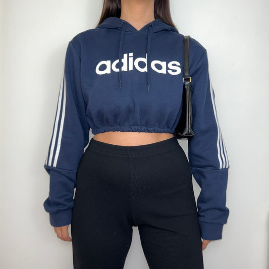 navy cropped hoodie with white adidas logos shown on a model wearing black trousers and a black shoulder bag