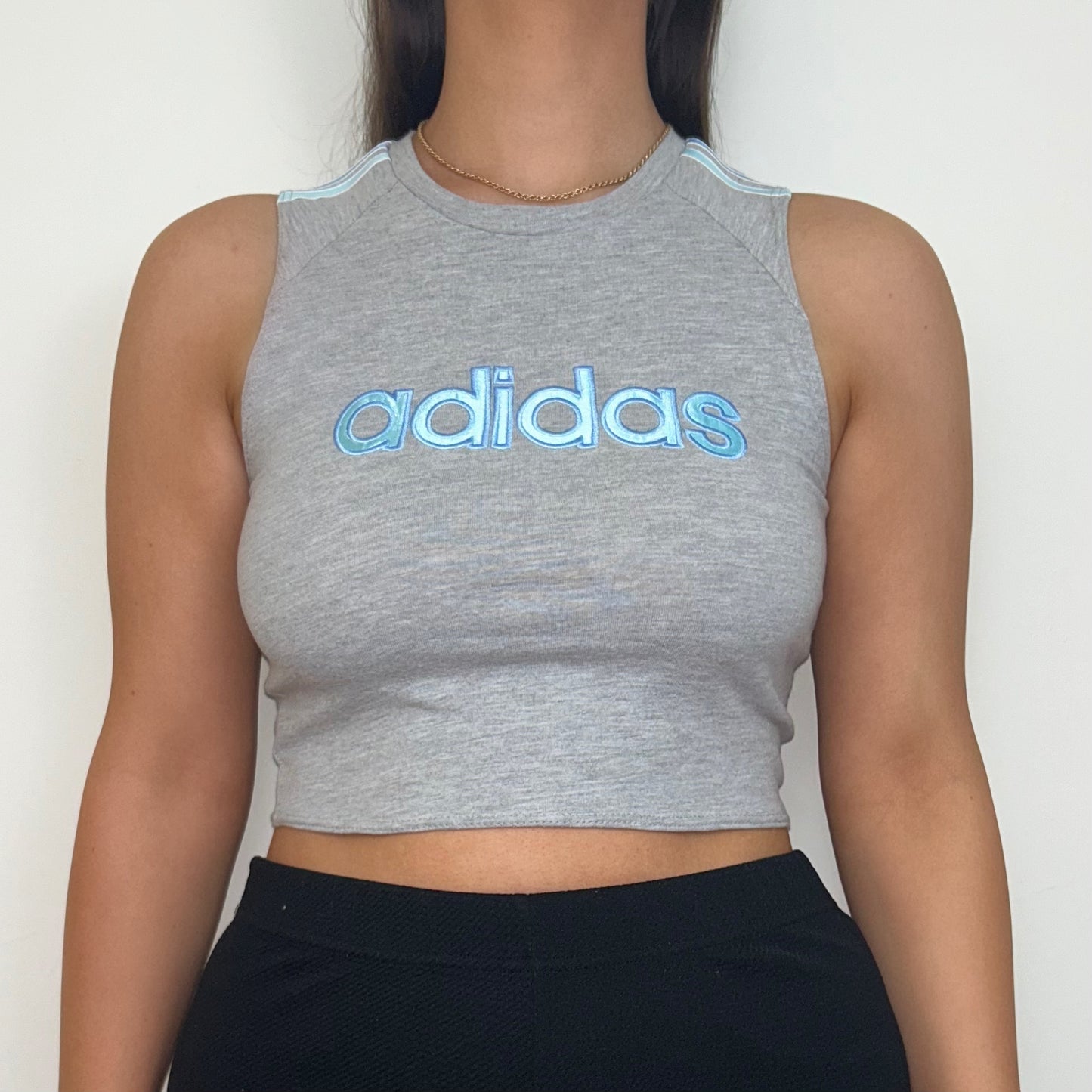 close up of grey short sleeve crop top with light blue adidas logo shown on a model wearing black trousers