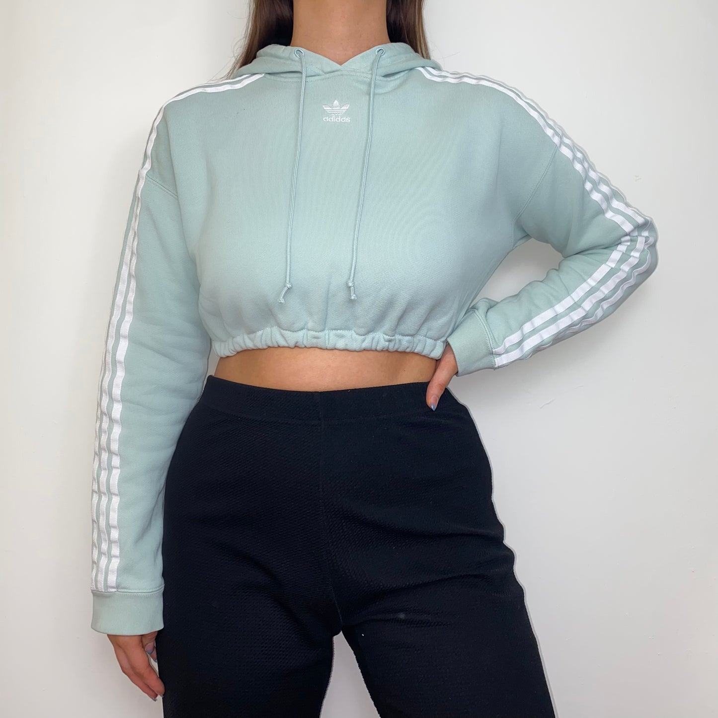 pastel green cropped hoodie with white adidas logo shown on a model wearing black trousers