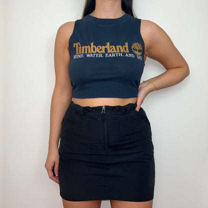 navy sleeveless crop top with orange and white timberland logo shown on a model wearing a black mini skirt