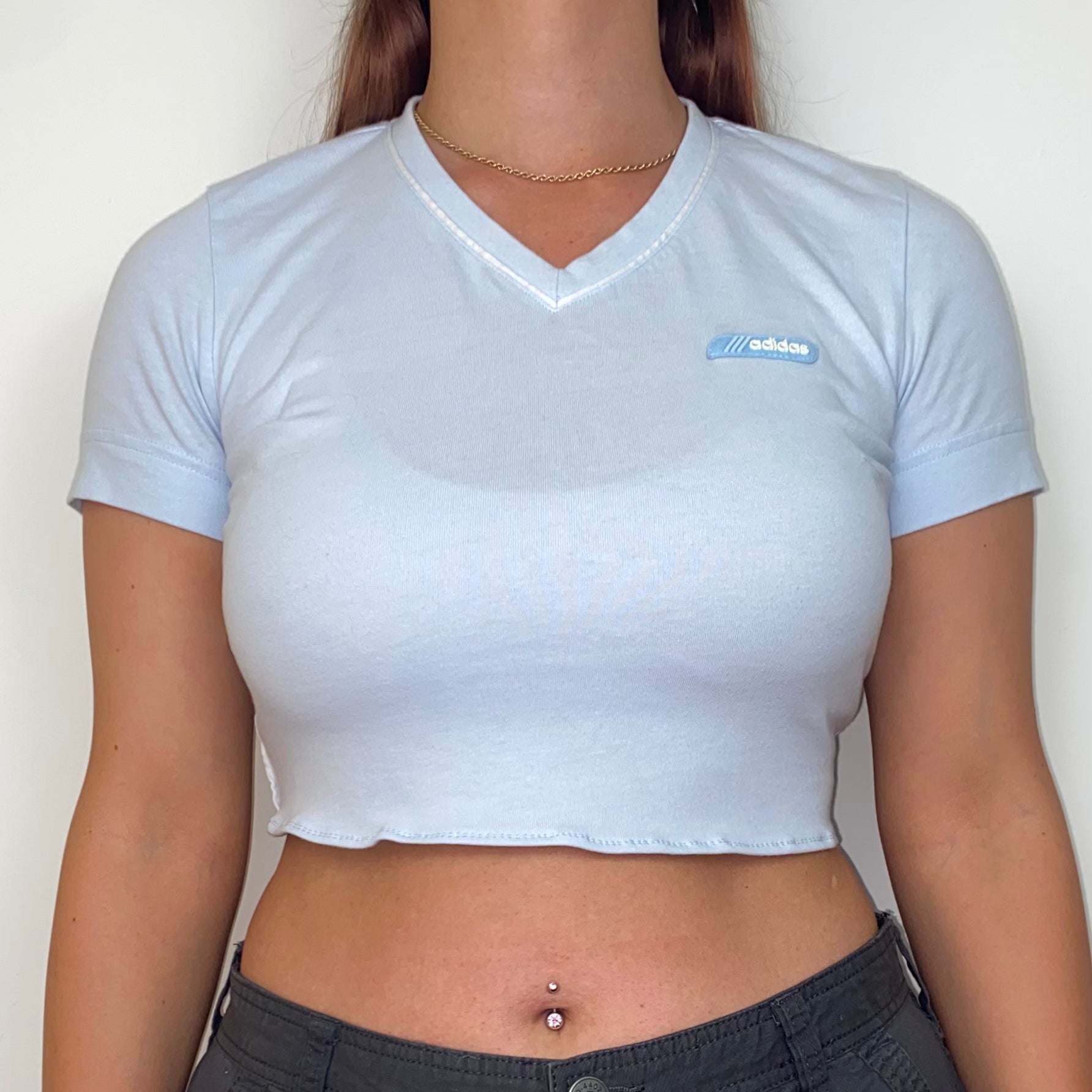 close up of a light blue short sleeve crop top with white adidas logo shown on a model wearing grey trousers