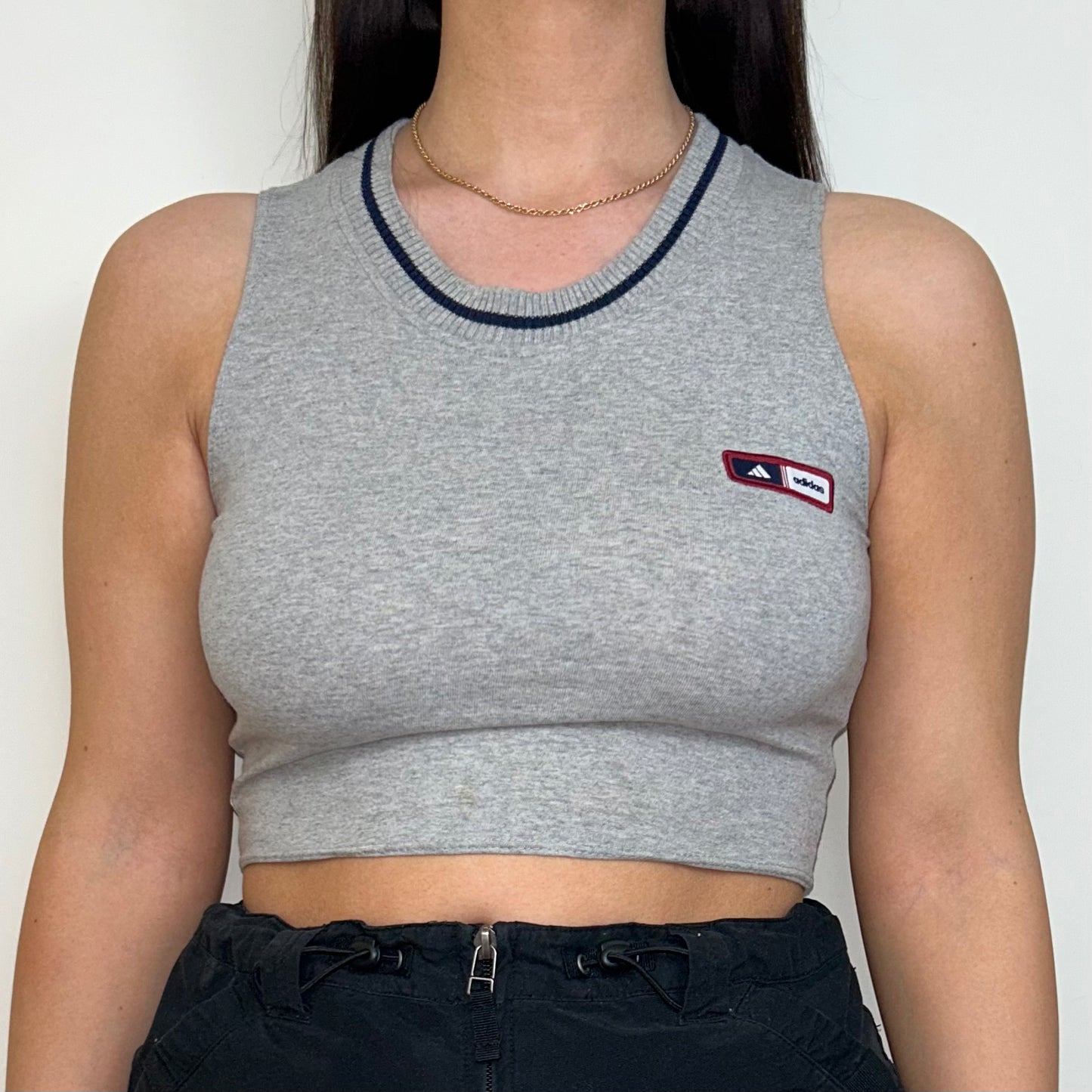 close up of grey sleeveless crop top with small adidas logo shown on a model wearing a black mini skirt