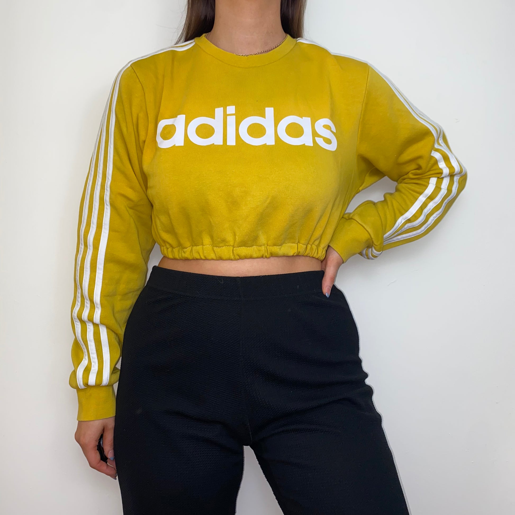 yellow cropped sweatshirt with white adidas logo shown on a model wearing black trousers
