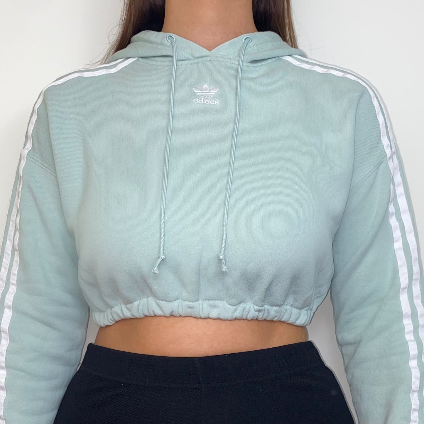 close up of a pastel green cropped hoodie with white adidas logo shown on a model