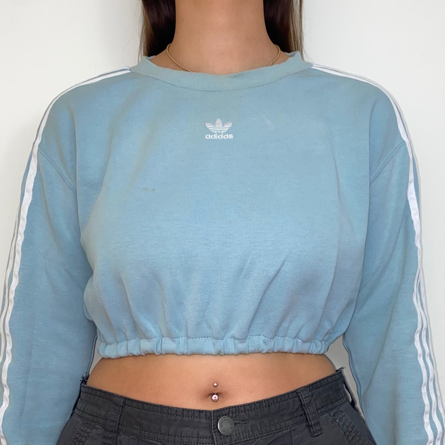 close up of light blue cropped sweatshirt with white adidas logo shown on a model wearing grey cargo trousers