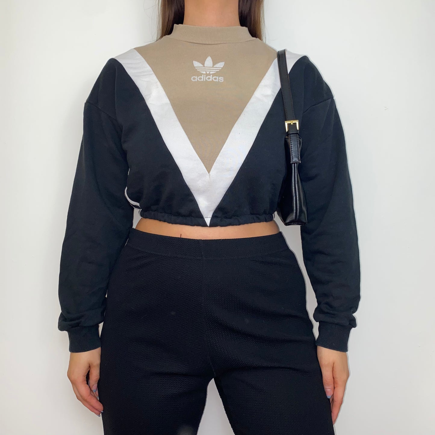 black and beige cropped hoodie with white adidas logo shown on a model wearing black trousers and a black shoulder bag