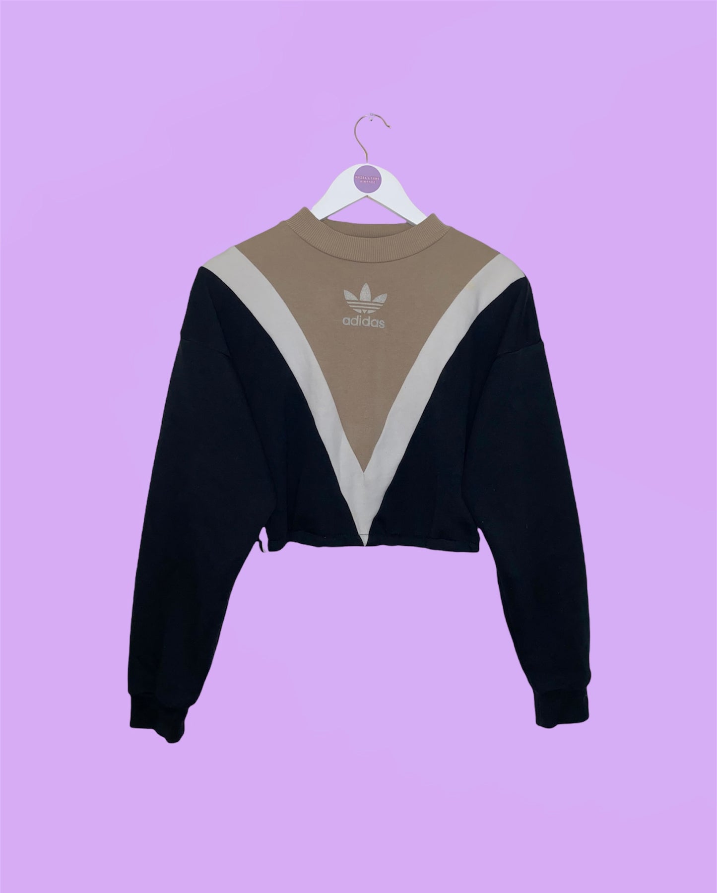 black and beige cropped sweatshirt with white adidas logo shown on a white clothes hanger on a lilac background