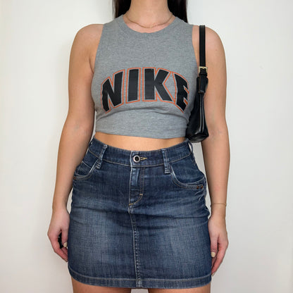 grey sleeveless crop top with orange and black nike logo shown on a model wearing a denim mini skirt and black shoulder bag