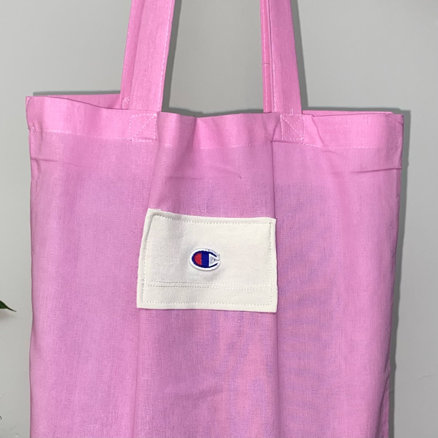 close up of light pink tote bag with blue and red champion logo