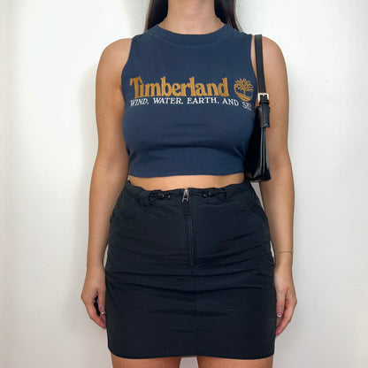 navy sleeveless crop top with orange and white timberland logo shown on a model wearing a black mini skirt and black shoulder bag