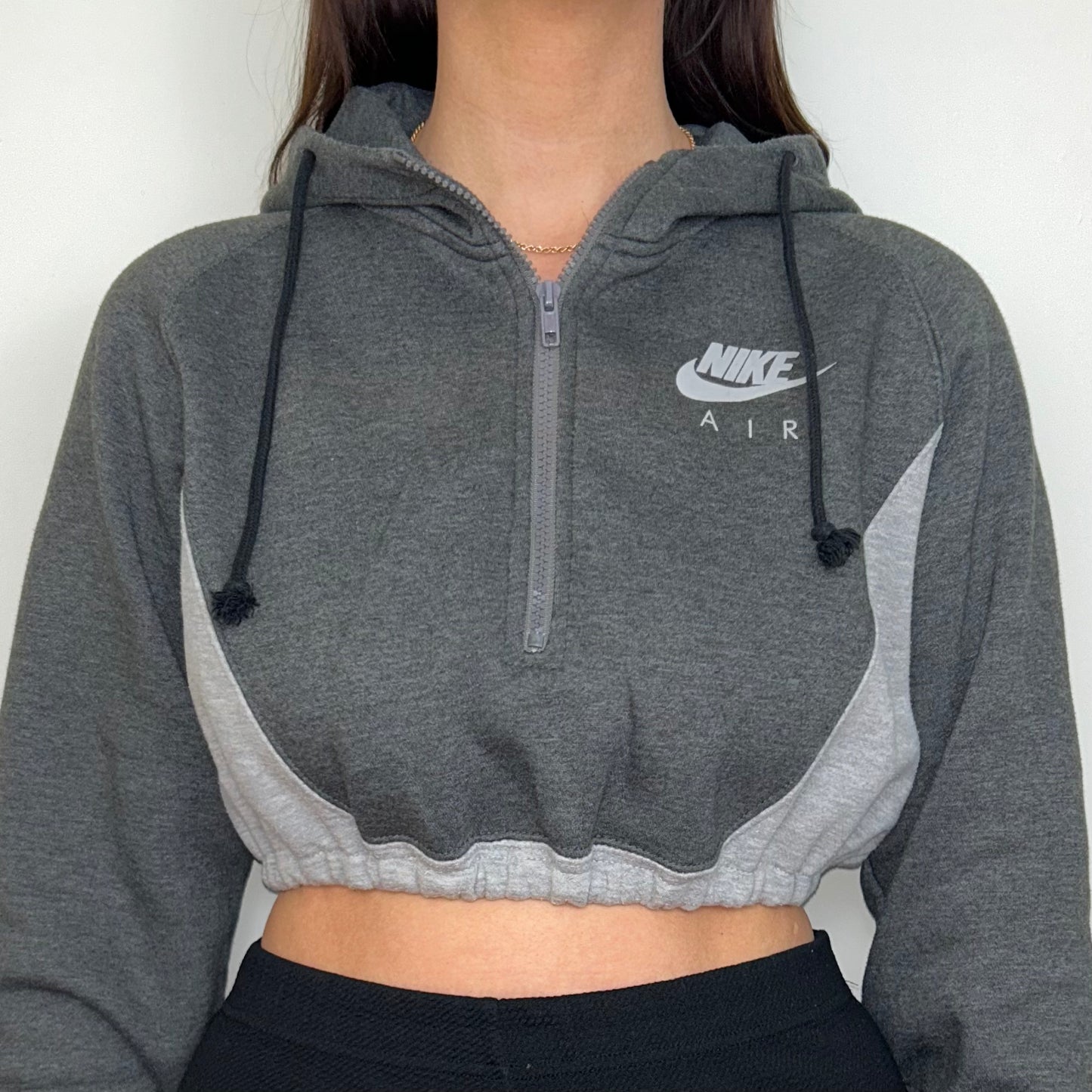 close up of grey 1/4 zip cropped hoodie with grey nike air logo shown on a model wearing black trousers