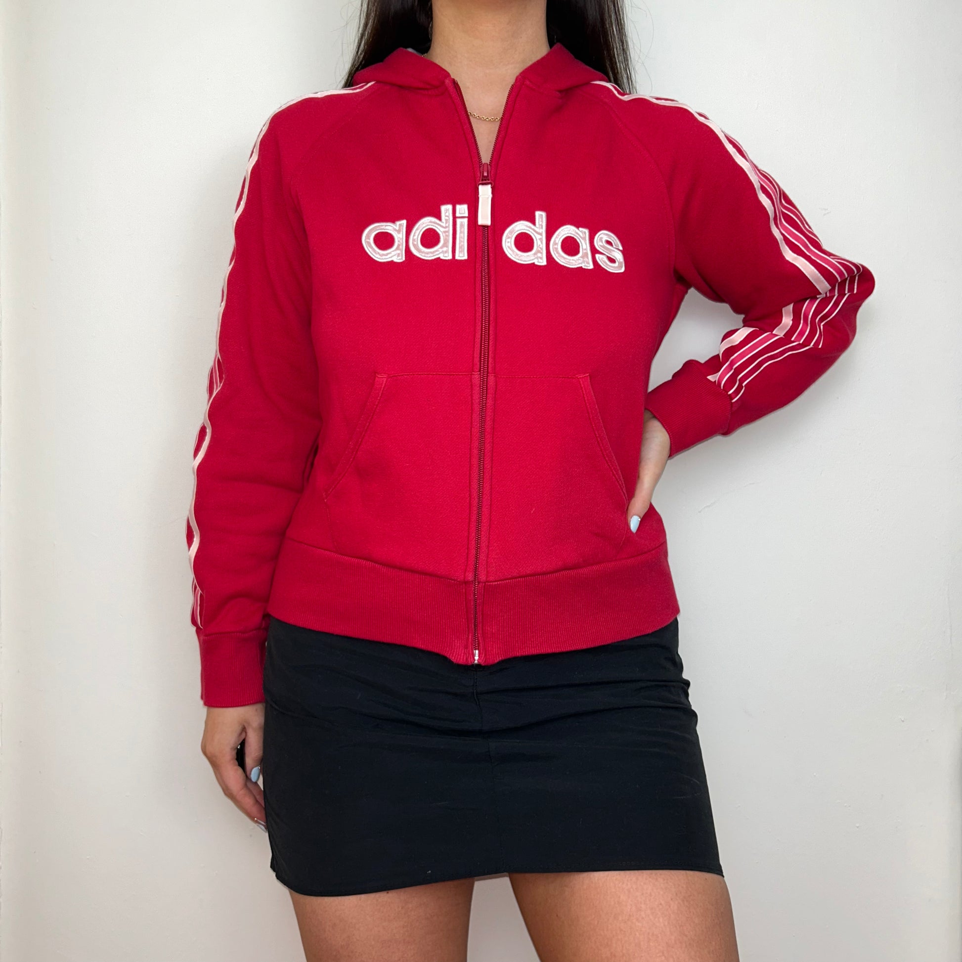 red zip up hoodie with big adidas text logo shown on a model wearing a black mini skirt