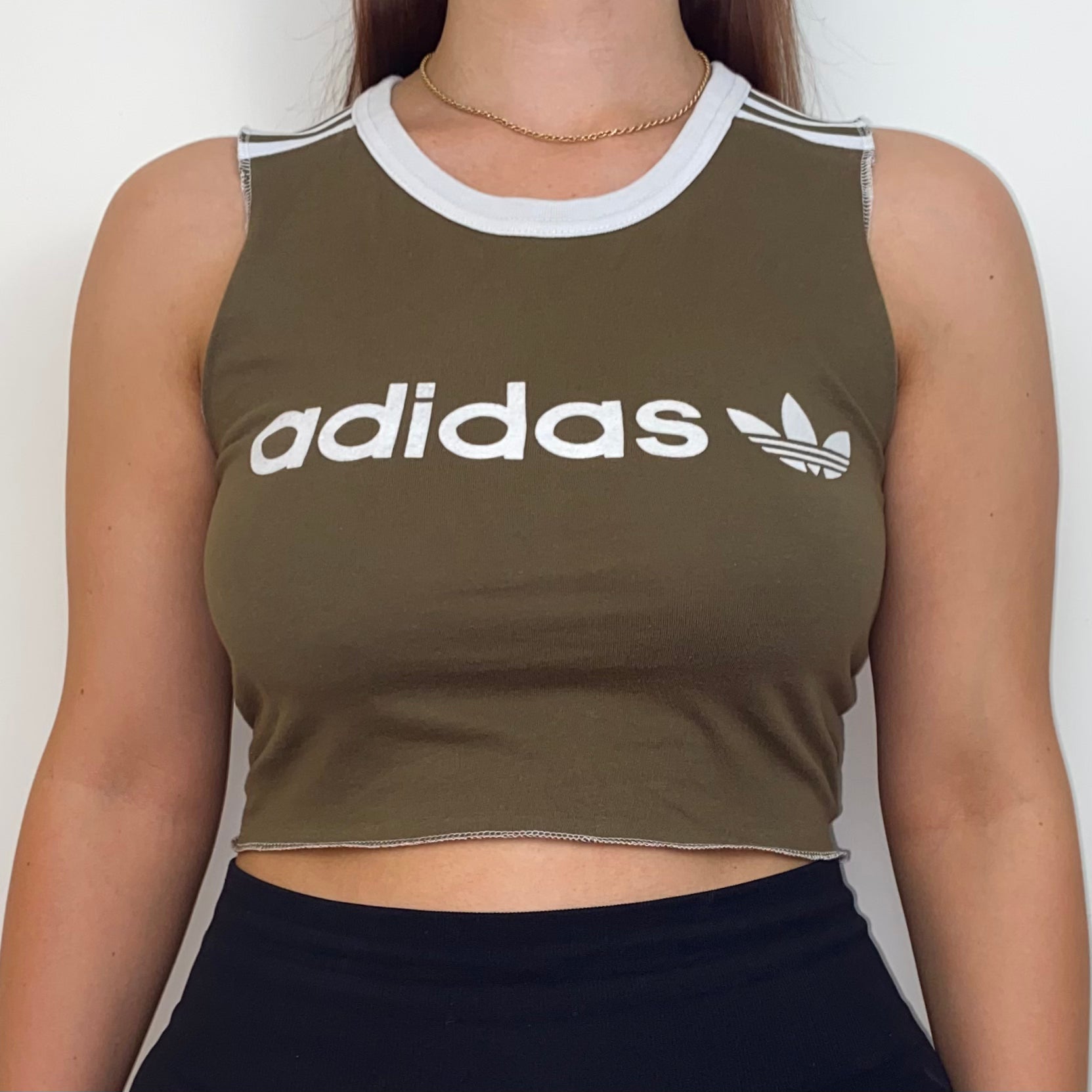 close up of khaki sleeveless crop top with white adidas logo shown on a model