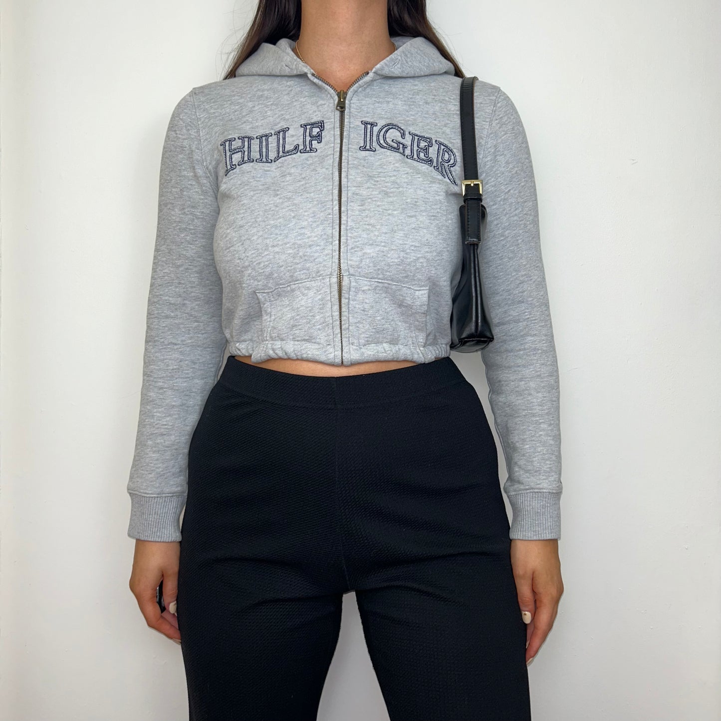 grey 1/4 zip cropped hoodie with navy hilfiger logo shown on a model wearing black trousers and a black shoulder bag