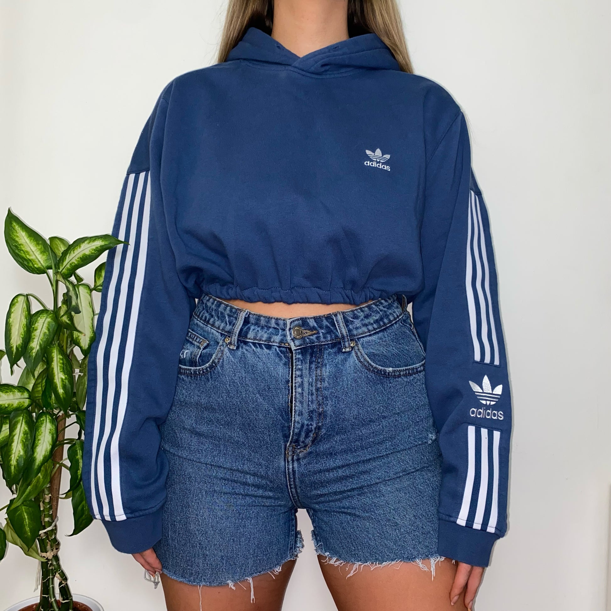 blue cropped hoodie with white adidas logo on chest and sleeves shown on a model wearing blue denim shorts